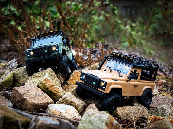 Dva RC Land Rovery Defender T98 V2 s LED rampou na kameňoch
